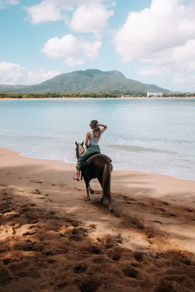 a woman riding on the back of a horse on a beach